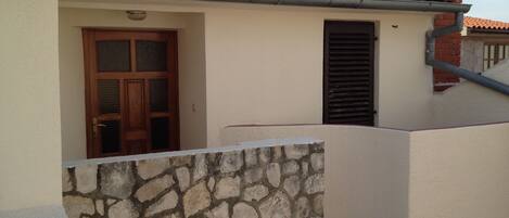 A building with a stone wall, a wooden door, and a window with shutters.