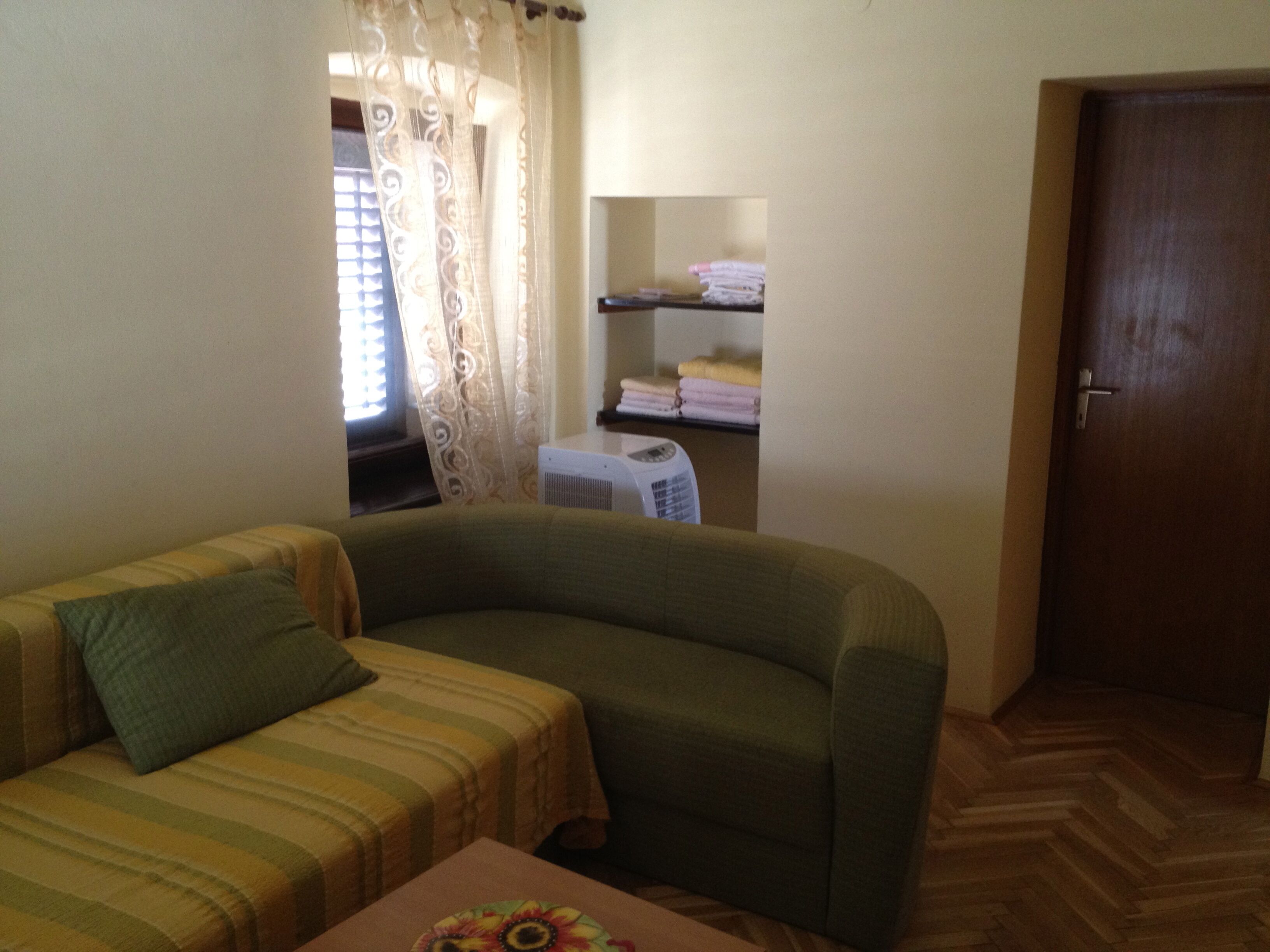 A room with a sofa, a small table, a heater, a door, and a window with curtains.