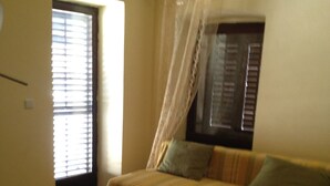 A room with a wooden herringbone floor, a sofa with striped cushions, a small table with a plate, and a window with blinds and a sheer curtain. - Apartment Iva - Great Vacation in the Center of Fazana, Istra (Croatia) (Fazana)