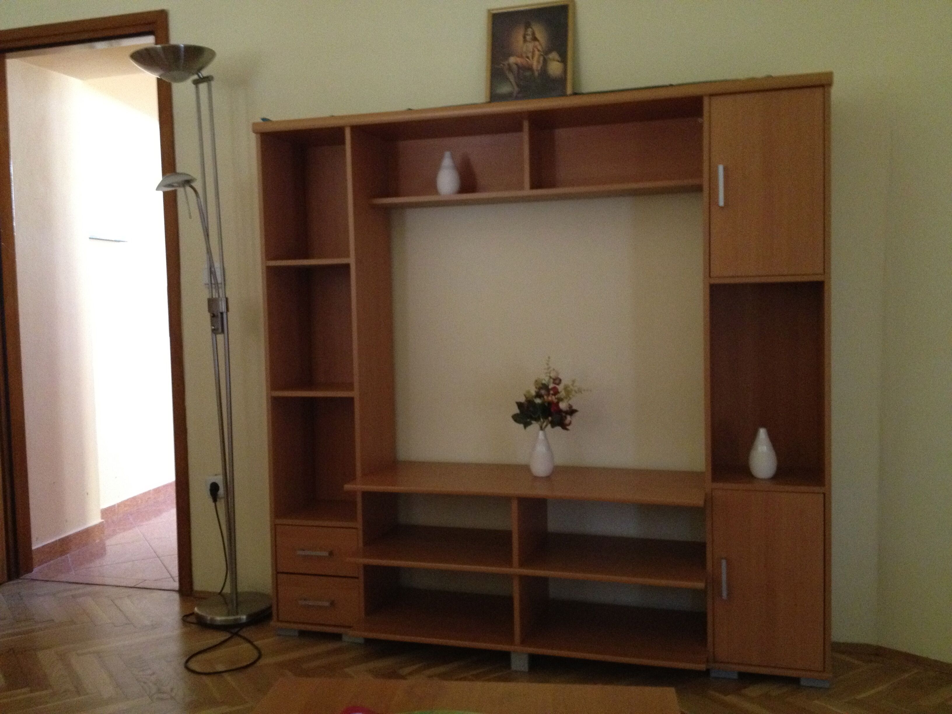 Ein Zimmer mit einem Holzkabinett, einer Stehlampe und einer Blumenvase.