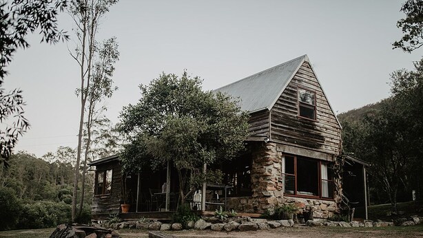 A rustic cabin with a stone foundation and wooden exterior, surrounded by trees and a grassy area. - Unique Rockhouse,  private jacuzzi, bush views (Rosebrook)