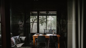 A cozy dining area with a wooden table and chairs, a view of trees through large windows, and a stone wall. - Unique Rockhouse,  private jacuzzi, bush views (Rosebrook)