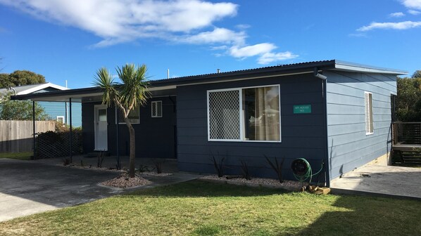 A single-story house with a dark blue exterior, a small front yard with a palm tree, and a sign reading "API HOUSE 145".