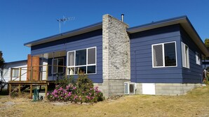 A modern two-story house with a stone chimney, large windows with white shutters, and a wooden deck. - API Leisure & Lifestyle St Helens (St Helens)