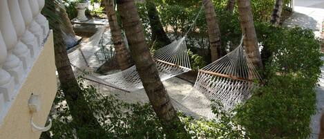 A hammock set up between palm trees in a courtyard with a white balustrade and a stone planter.