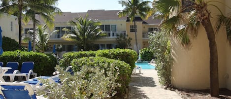 A poolside area with lounge chairs, palm trees, and a building with balconies.