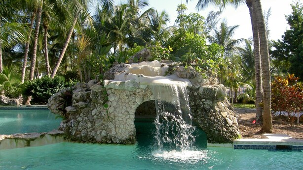 Une piscine agrémentée d’une formation rocheuse naturelle et d’une cascade.