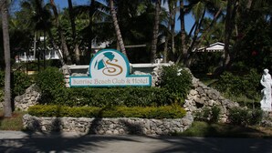 Une enseigne indiquant l’emplacement du Sunrise Beach Club & Hotel, entourée de palmiers et d’une statue.