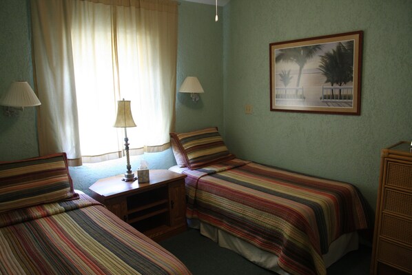 A room with two single beds, a nightstand, a lamp, a painting, and a window with curtains. - Atlantis Paradise Island Beach Area Luxury Apartment (Nassau)