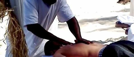 A beach scene with a person receiving a massage on a white mat.