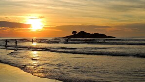 A beach scene with waves, a sunset, and a distant island. - Guaruja, Pitangueiras beach, flat with services. (Guarujá)