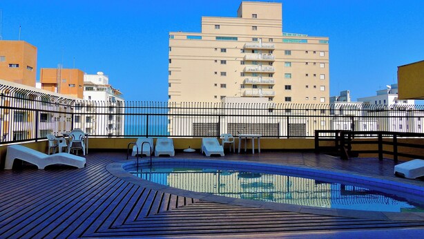 A rooftop pool area with lounge chairs and a pool, surrounded by a metal fence, with buildings in the background. - Guaruja, Pitangueiras beach, flat with services. (Guarujá)