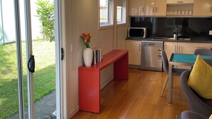 A modern kitchen with a microwave, sink, and cabinets. There is a dining table with chairs and a bench. A sliding glass door leads to a patio with a garden. - Lone Pine Retreat - Bright, airy spaces, full kitchen, kids & pets welcome! (Enoggera)