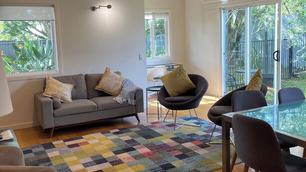 A modern living room with a grey sofa, a glass dining table, and a ceiling fan. - Lone Pine Retreat - Bright, airy spaces, full kitchen, kids & pets welcome! (Enoggera)