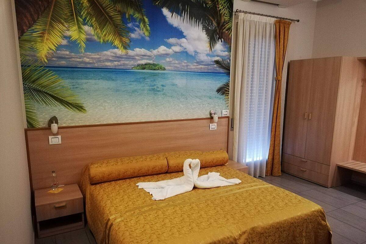 A hotel room with a bed, a nightstand, a wardrobe, and a mural of a beach scene.