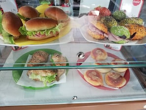 A display case with various food items including sandwiches and pastries. - Motel Karibe (Fratta Polesine)