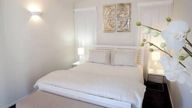 A neatly arranged bedroom with a bed, bedside tables, and a decorative wall piece. - Lavender Apartment 2  One bedroom Apartment (Coromandel Township)