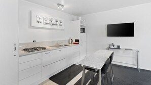 A modern kitchen with white cabinetry, a gas stove, a sink, and a flat-screen TV mounted on the wall. - Lavender Apartment 2  One bedroom Apartment (Coromandel Township)
