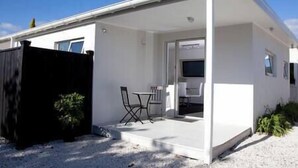 A modern single-story house with a covered patio, a small table and chairs, and a TV mounted on the wall. - Lavender Apartment 2  One bedroom Apartment (Coromandel Township)
