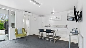 A modern kitchen with white cabinets, a dining area with a table and chairs, and a grey carpeted floor. - Lavender Apartment 2  One bedroom Apartment (Coromandel Township)