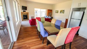 A dining area with a wooden table and colorful chairs, a fireplace, and a kitchen with a refrigerator. - BLUE HILLS RISE: Bright (Bright)
