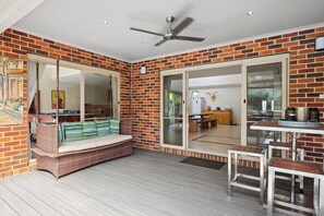 A room with a brick wall, a ceiling fan, a sliding glass door leading to an outdoor area, and a seating area with a bench and a table.