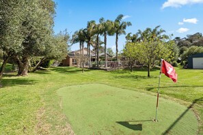 A golf course with a putting green, trees, and a house in the background.