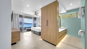 A modern hotel room with a large bed, a wooden wardrobe, a bathroom with a sink and mirror, and a view of the sea. - The Elite F208 Hamilton Island by HamoRent (Hamilton Island)