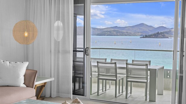 A modern hotel room with a balcony overlooking a scenic lake and mountains. - The Elite F208 Hamilton Island by HamoRent (Hamilton Island)