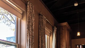 Une pièce avec un banc en bois près d’une fenêtre, une chaise et une lampe fixée au mur.