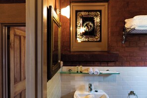A bathroom with a wooden door, a glass shelf with toiletries, a sink, and a towel rack.