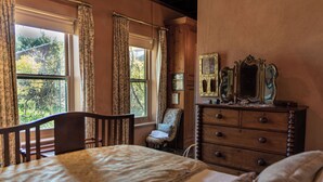 Une chambre à coucher avec un lit, une commode, une chaise et une fenêtre avec des rideaux.