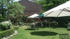 Un jardin bien entretenu, avec un mur en briques, une table entourée de chaises et un grand parasol.