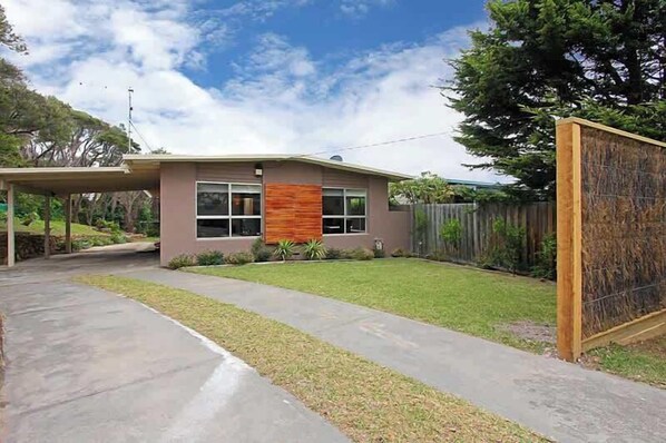 A modern two-story house with a covered patio, a fenced backyard, and a wooden fence.