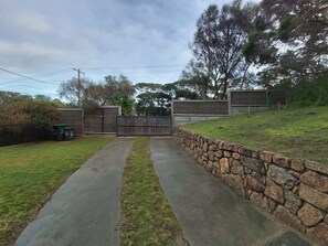 Ein gepflasterter Weg führt zu einem verschlossenen Eingang, einer Seite eine Steinmauer, auf der anderen eine Rasenfläche.