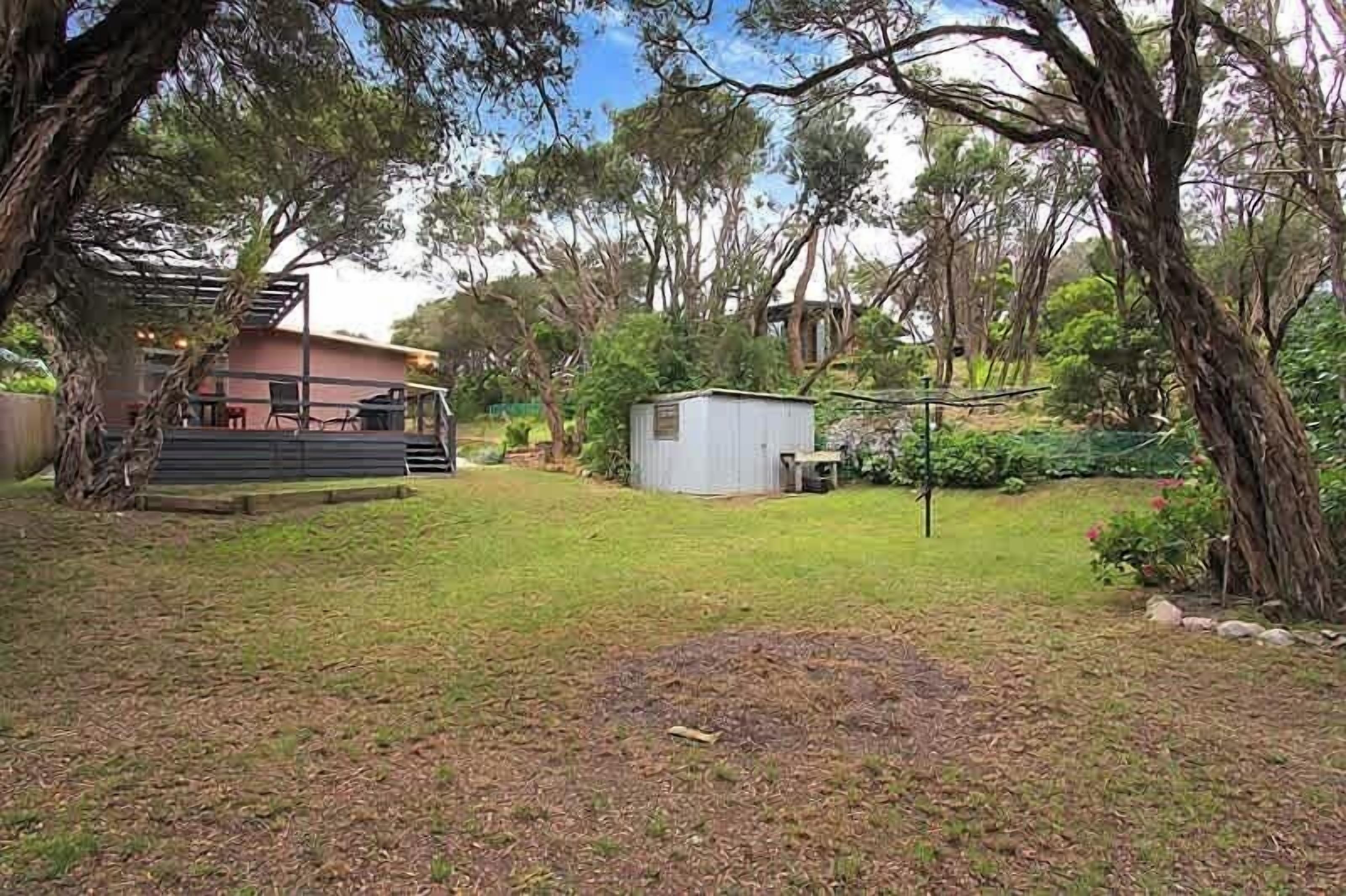 A backyard with a small shed, a wooden deck, and a house in the background.