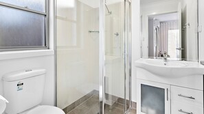 A modern bathroom with a toilet, a glass shower enclosure, a sink, and a mirror.