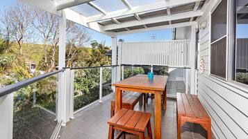 A covered outdoor area with a wooden table and benches, a glass railing, and a view of the surrounding landscape.