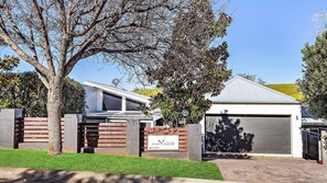 A modern two-story house with a garage, a well-maintained lawn, and a tree in the foreground.