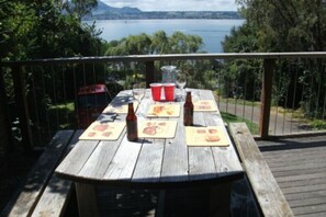 Una terraza de madera con una mesa dispuesta para una comida, con vistas a un cuerpo de agua y árboles.
