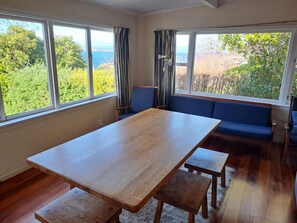 Una habitación con una mesa de madera, bancos, un sofá azul y ventanas amplias que ofrecen vistas a zonas verdes y una masa de agua.