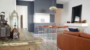 Ein modernes Wohnzimmer mit einem Holztisch, einem orangefarbenen Sofa und einem Essbereich mit Stühlen und einem weißen Regal.