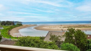 A coastal view with a sandy beach, a curved water body, and residential buildings in the foreground. - Shirl's By The Sea - beach at your doorstep (Gerroa)
