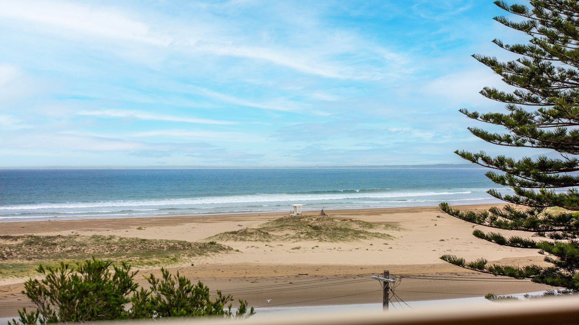 Une vue sur la plage, avec un ciel dégagé, un rivage sablonneux et une petite construction sur la plage.