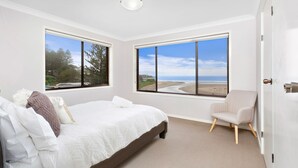 A bedroom with a bed, a chair, and two large windows offering a beach view. - Shirl's By The Sea - beach at your doorstep (Gerroa)