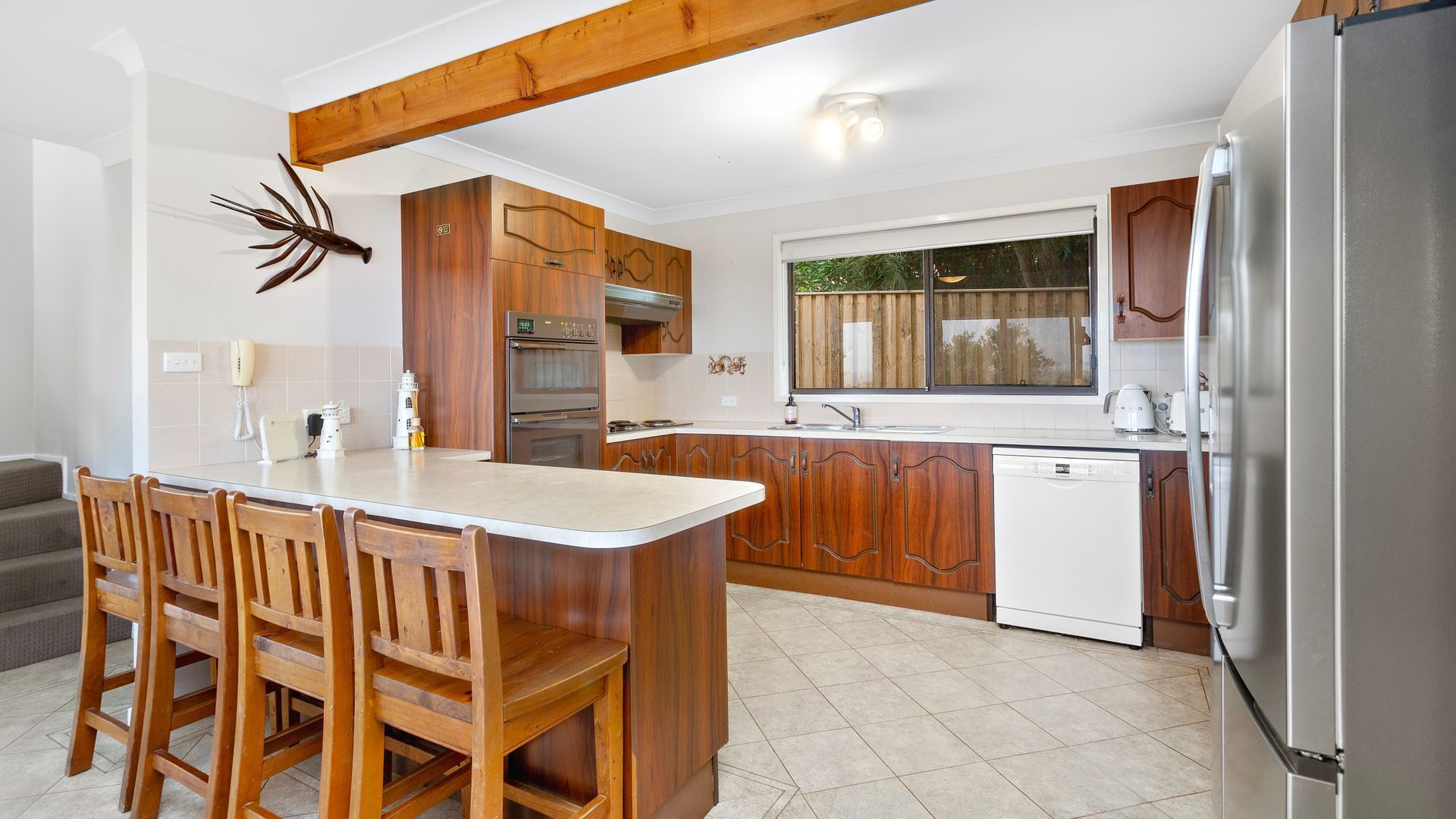 A kitchen with wooden cabinets, a built-in oven, a dishwasher, and a large island with chairs.