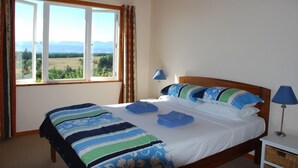 Ein Schlafzimmer mit einem großen Bett, zwei Nachttischlampen und Blick auf eine grüne Landschaft durch ein Fenster.