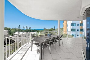 Un balcon avec une table et des chaises, une vue sur la mer et, au loin, des bâtiments modernes.