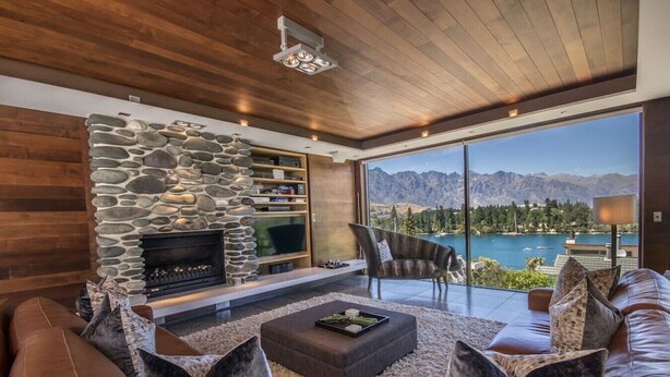 Un salon moderne doté d’une cheminée en pierre, d’un canapé en cuir et d’une grande fenêtre offrant une vue sur un lac de montagne.
