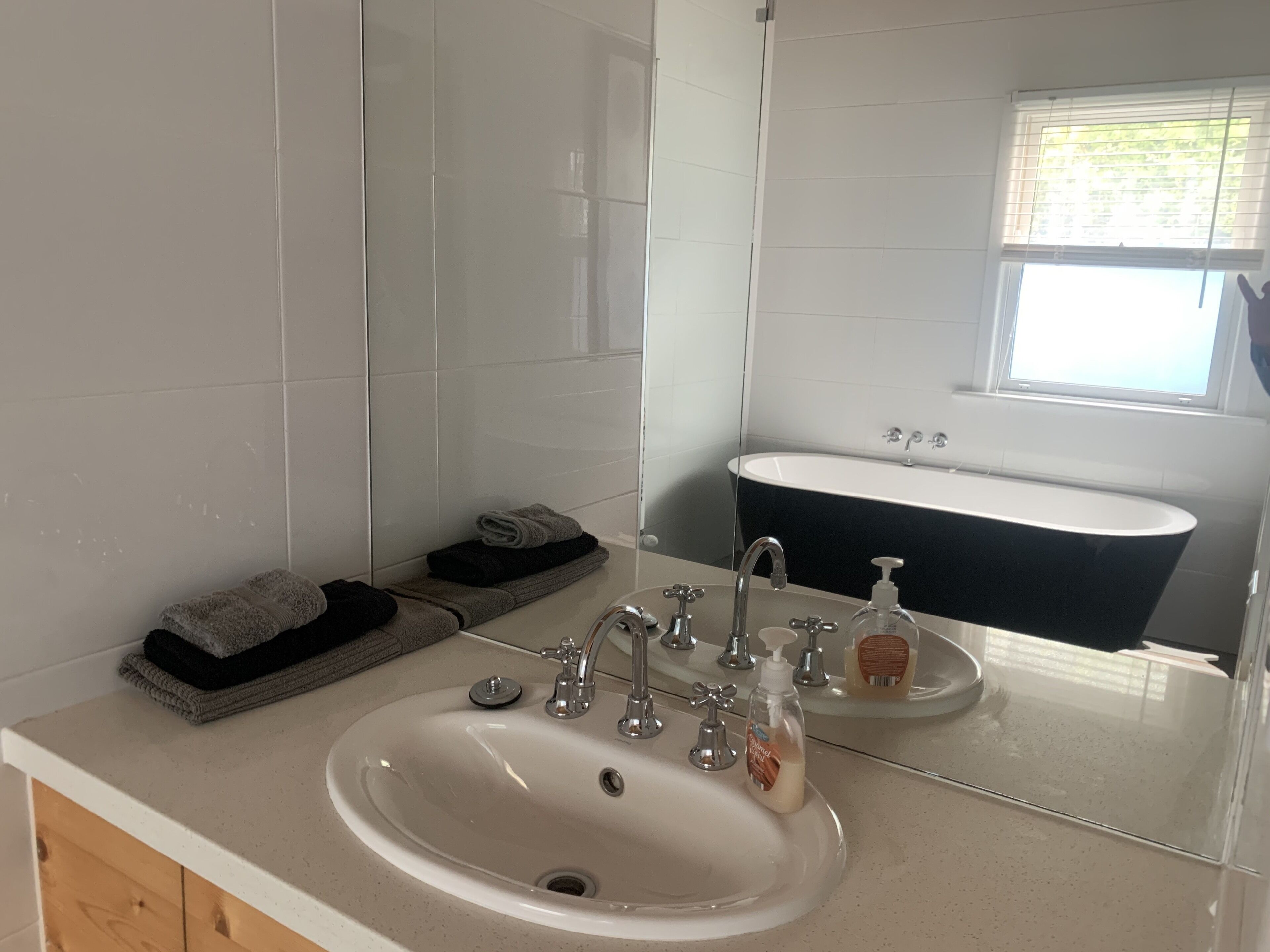 Ein Badezimmer mit einem weißen Waschbecken, einer schwarzen Badewanne und einem Spiegel, der den Raum widerspiegelt.